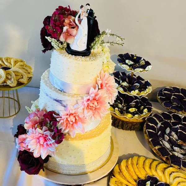 A three-tiered wedding cake with a bride and groom topper, surrounded by Filipino pastries.