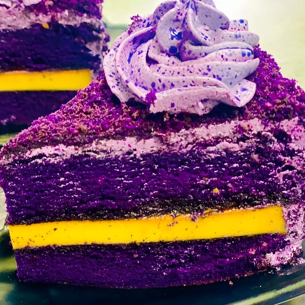 Close-up of a vibrant purple ube cake slice with a bright yellow custard layer and purple frosting.