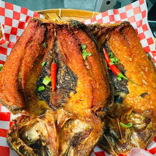 Two crispy fried Filipino milkfish, garnished with red chilies and green onions, on checkered paper.