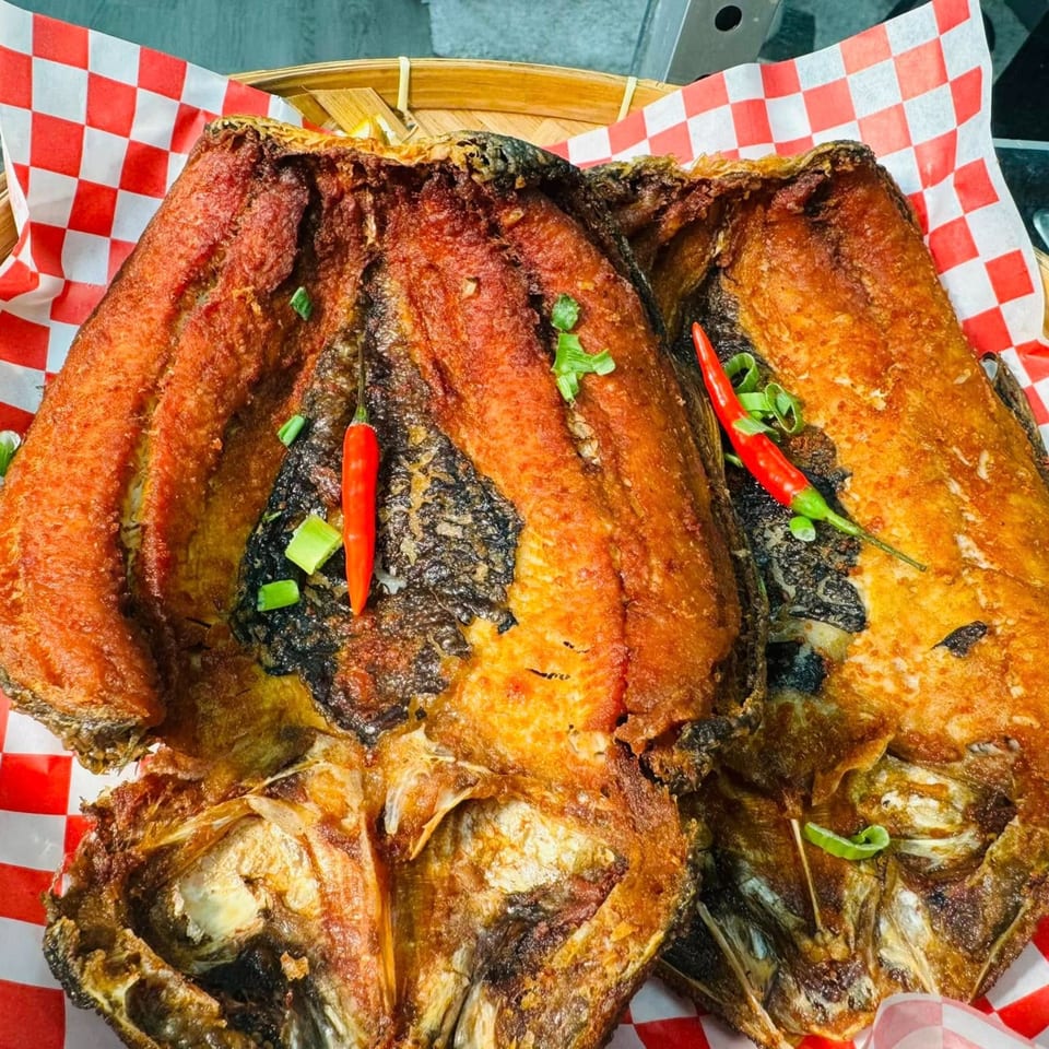 Two crispy fried Filipino milkfish, garnished with red chilies and green onions, on checkered paper.