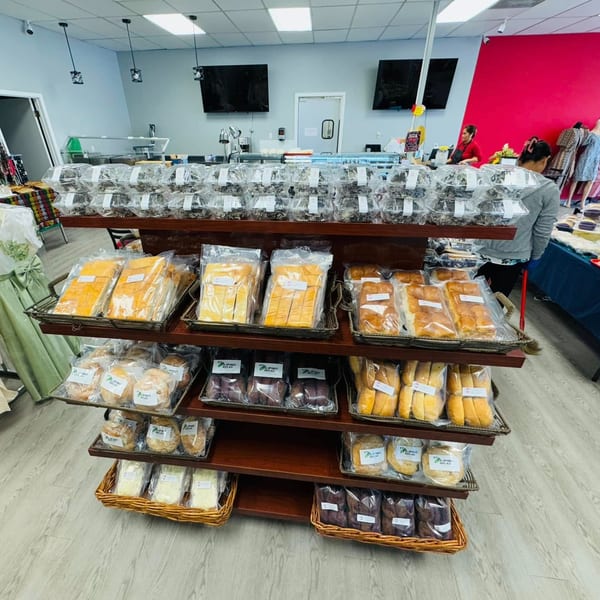 A Filipino bakery display rack filled with various packaged breads and pastries, with customers in the background.