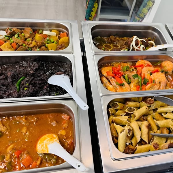 A buffet of Filipino dishes including shrimp, lumpia, and various stews in metal serving trays.