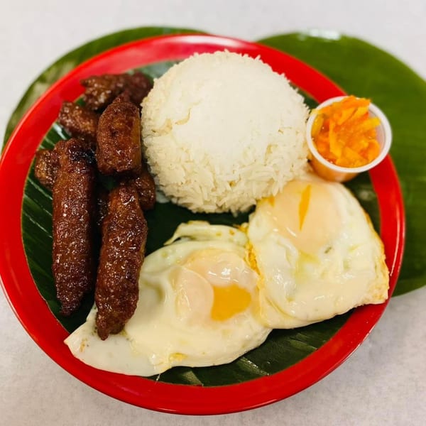 Filipino longganisa sausages, fried eggs, rice, and pickled papaya on a red plate with banana leaf.