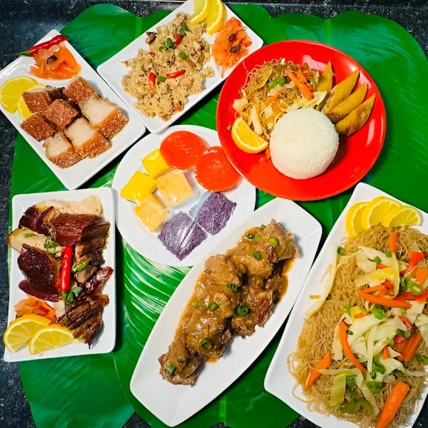 A vibrant spread of Filipino dishes, including crispy pork, noodles, rice, and desserts, on banana leaves.
