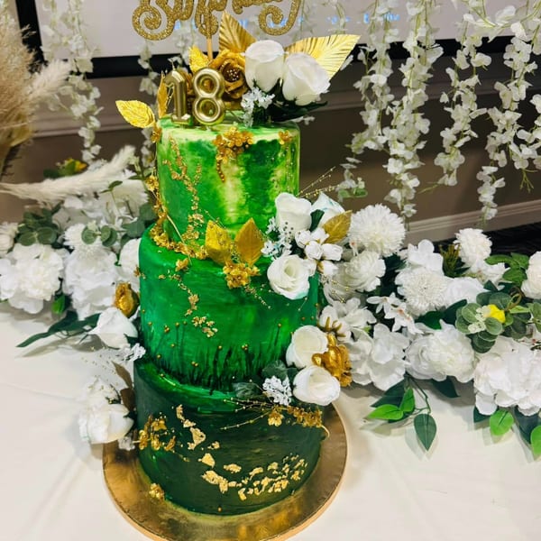 A three-tiered green cake with gold accents, white roses, and an "18" candle, surrounded by white flowers.