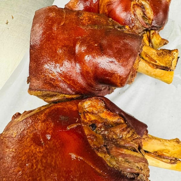 Two crispy Filipino pork hocks, or crispy pata, with bones visible, on white parchment paper.