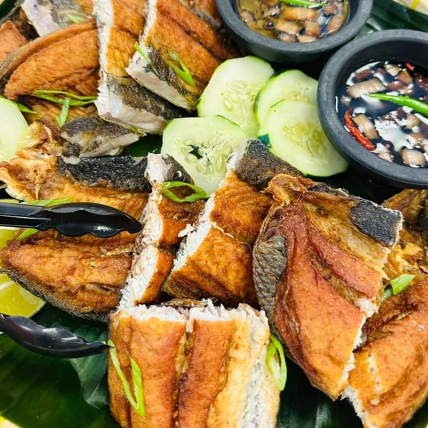 Filipino fried fish pieces with cucumber slices and two small bowls of dipping sauce.