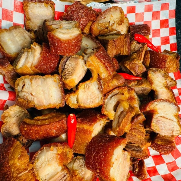 Crispy Filipino lechon kawali pork belly pieces with red chili peppers on red and white checkered paper.