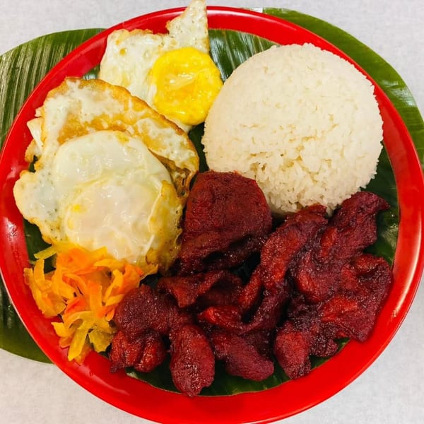 Filipino tocino, fried eggs, and rice on a red plate with banana leaf.