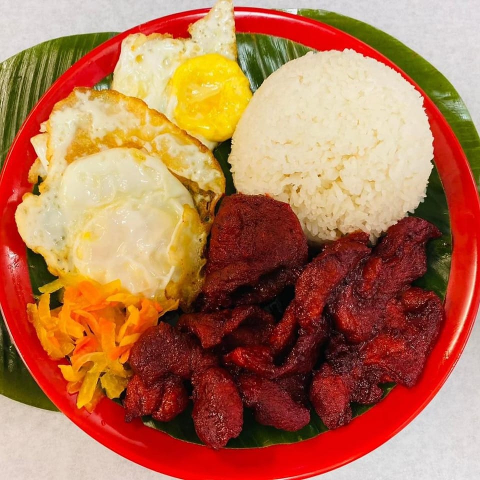 Filipino tocino, fried eggs, and rice on a red plate with banana leaf.