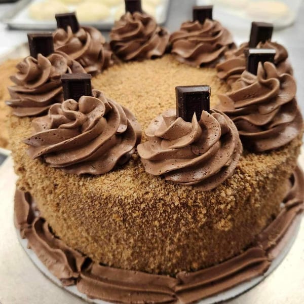 A chocolate cake with chocolate frosting swirls and chocolate bar pieces on top, with a crumb coating.
